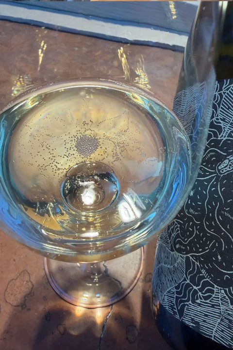 A clear wine glass with a sparkling wine viewed from above on a brown surface, with a dark wine bottle.